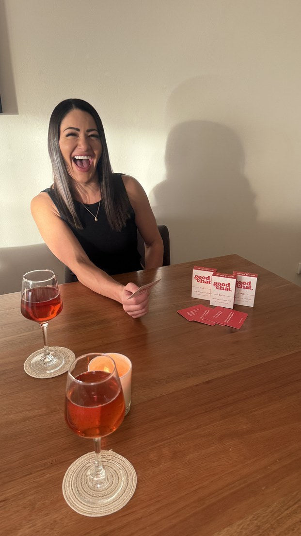 Woman laughing at a wooden table with Dates conversation cards in window light