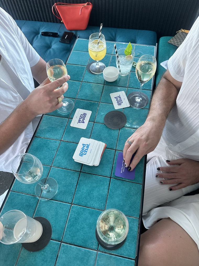 Overhead turquoise-tiled table with drinks and Good Chat cards mid-game