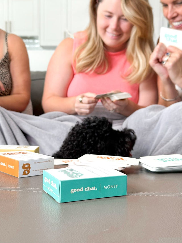 Two friends and a poodle playing with the Money conversation deck on a bright couch