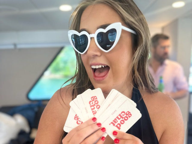 Woman in heart sunglasses playfully fanning cards at a bright party