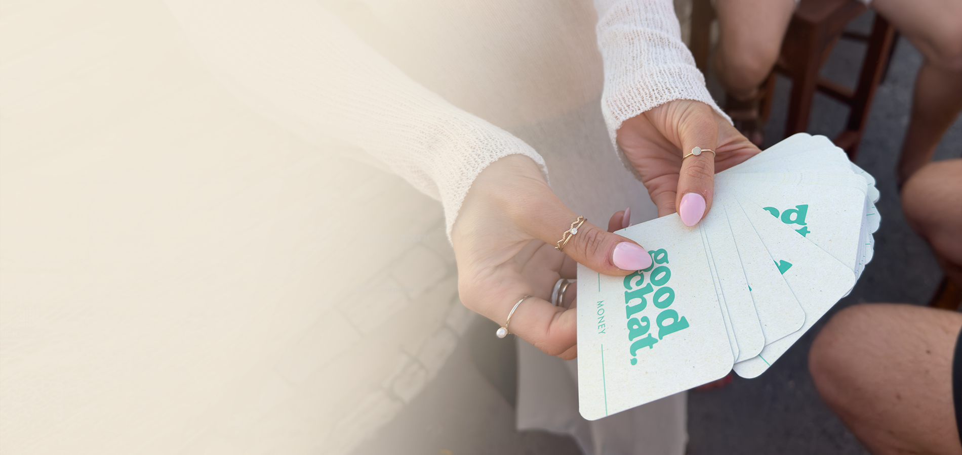 Hands holding playing cards with 'Good Chat' conversation cards on a neutral background