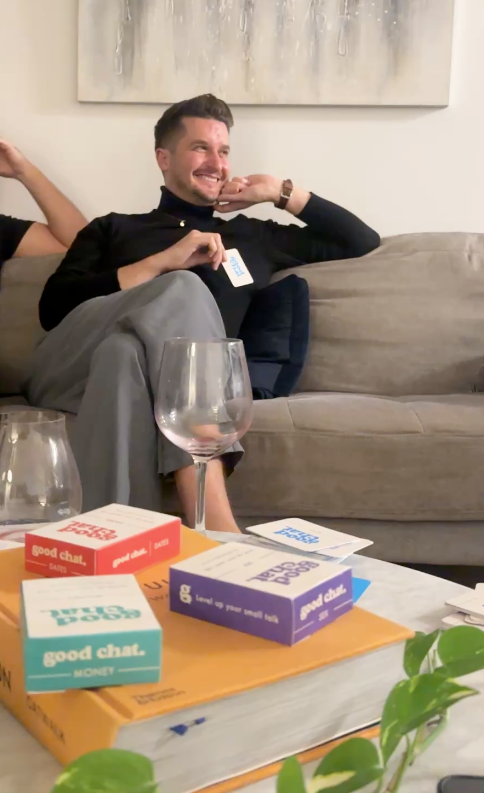 Person sitting on a couch with 'good chat' product boxes and a glass of wine.