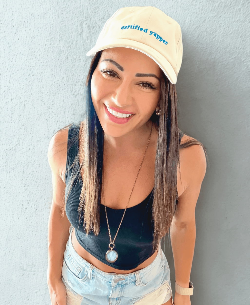 Woman wearing a beige cap with 'certified yapper' text against a plain background