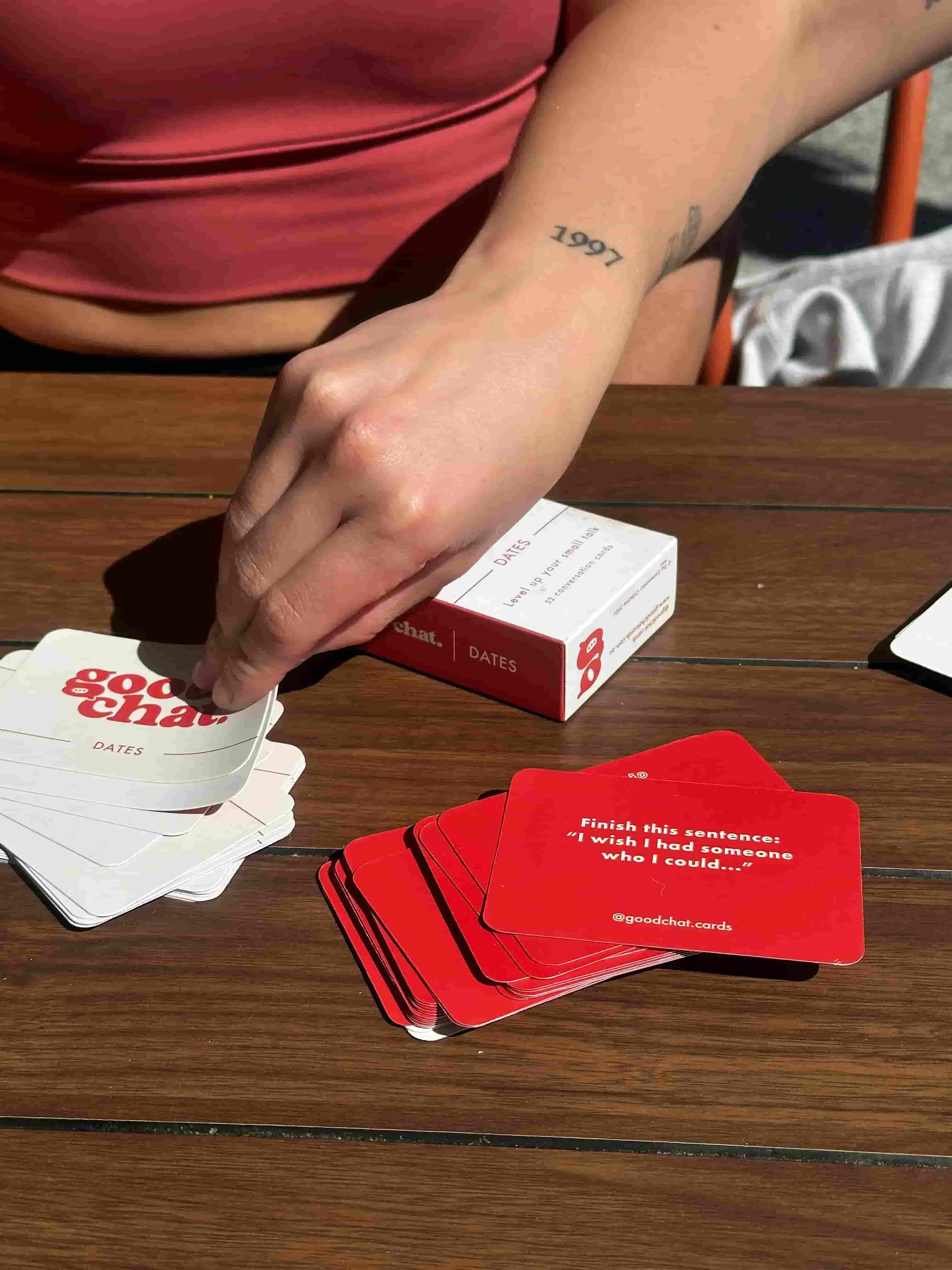 Person playing a card game with red and white cards on a wooden table.